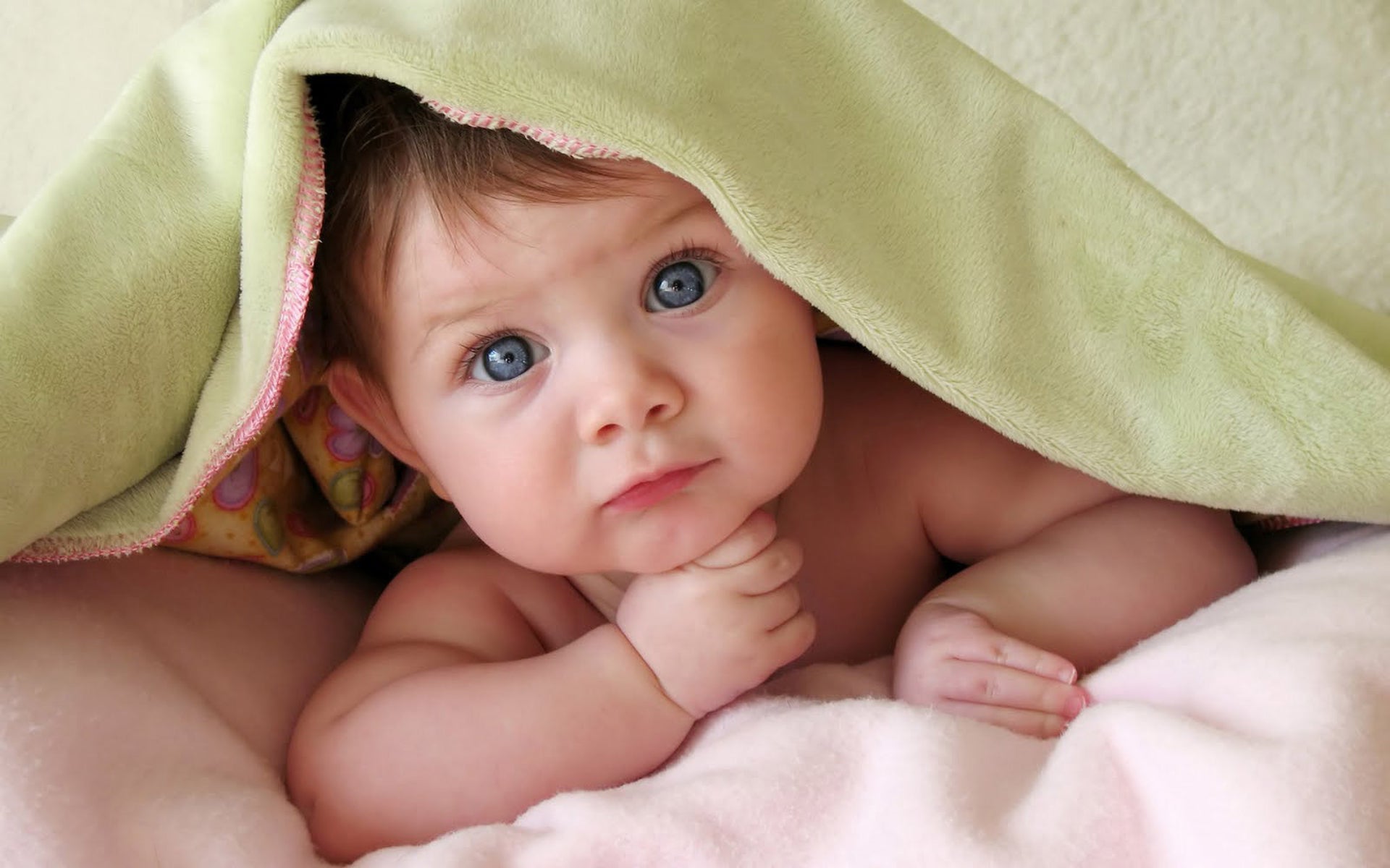 a baby wearing barrier lotion to protects its skin, laying down under a blanket with their head popping out, looking at the camera preciously