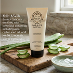 A tube of Skin Saver Labs Barrier Lotion stands on a wooden board with aloe vera slices and a bowl of aloe gel in a softly lit bathroom-like setting. Text on the left describes the lotion's botanical ingredients.