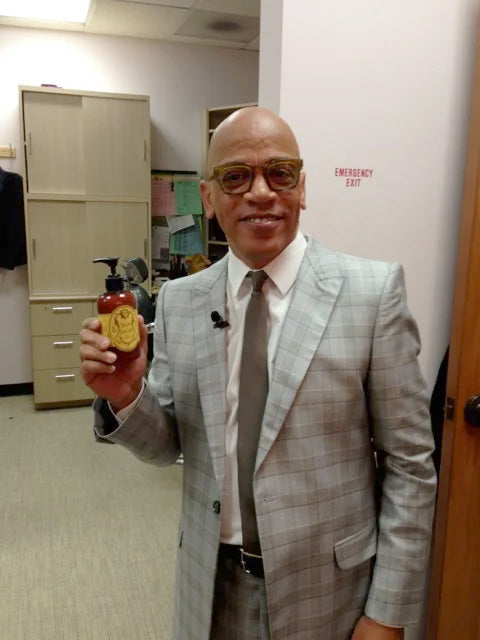 Ricky Minor in a grey suit holding a bottle of Skin Saver Barrier Lotion