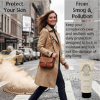 A woman in a beige trench coat walks across a city crosswalk while wearing a brown leather crossbody bag. She is walking past a manhole emitting steam. She is wearing Barrier Lotion to protect her skin from smog and pollution and to keep it hydrated as she explores the city.
